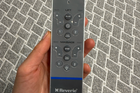 Hand holding a Reverie remote control against a textured gray background