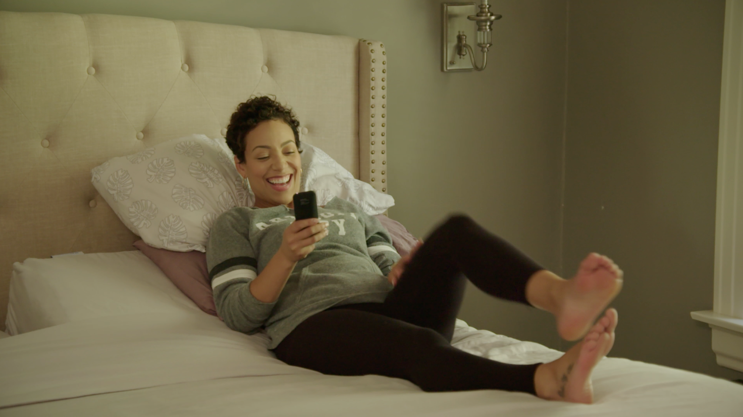 Woman sitting on an adjustable bed using a smartphone in a bedroom setting.